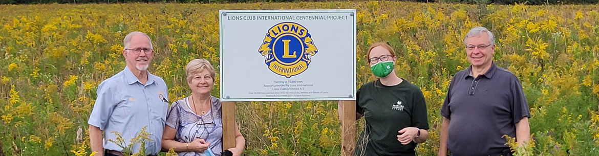 Paul De Cloet, Josiane De Cloet, Liv Monck-Whipp, Ron Keba stand in front of sign to commemorate Lion's Club centennial tree planting project. Photo by NCC.