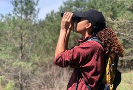 Picture of Misha Golin using a pair of binoculars to see an eastern phoebe (Photo by Jaide Wilkinson)