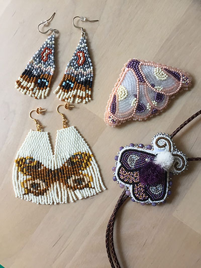 Four moth beadwork pieces (From top left clockwise:  xʷəlməxʷ beadwork @xwelmexwbeadwork, Reags Beads @reagsbeads (pink moth pin), Story Bead Creations @manidoominens_adizookaan (moth bolo), Diving Loon Co. (@divingloonbeads))