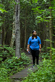 A visitor enjoying a leisurely stroll on a boardwalk in a lush, green forest (Photo by Nila Sivatheesan/NCC staff)